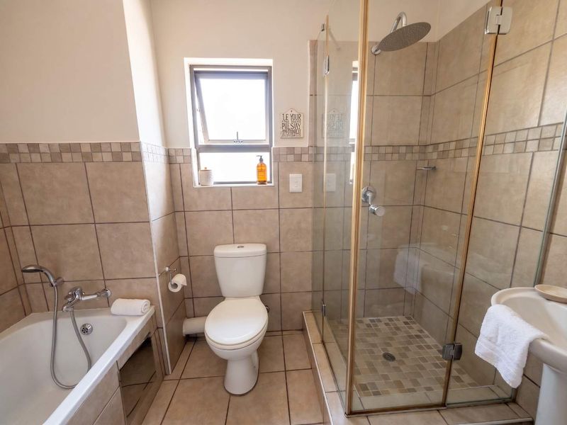 A well-maintained bathroom featuring a bathtub, separate glass-enclosed shower, toilet, and pedestal basin with neutral floor-to-ceiling tiling.