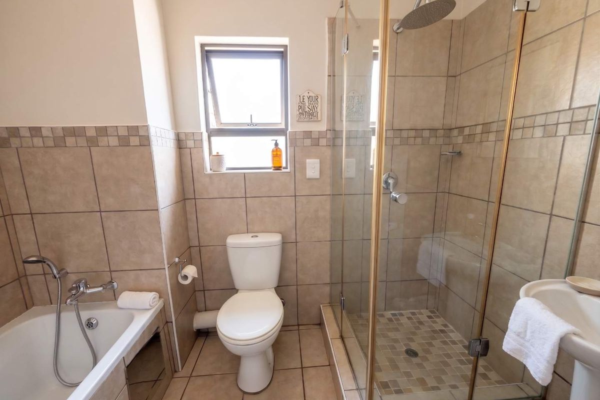 A well-maintained bathroom featuring a bathtub, separate glass-enclosed shower, toilet, and pedestal basin with neutral floor-to-ceiling tiling.