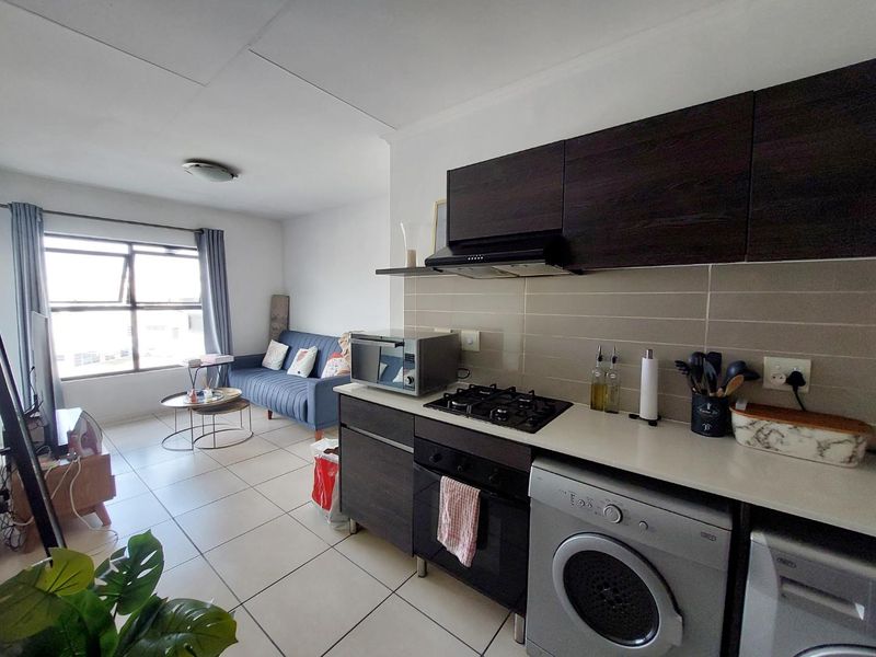 Open-plan living area featuring a modern kitchen with dark cabinetry, gas hob, built-in oven, and tiled flooring, seamlessly flowing into the lounge space.