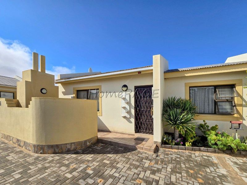 Front elevation of the townhouse featuring a paved driveway, secure entrance gate, and a built-in outdoor braai area.