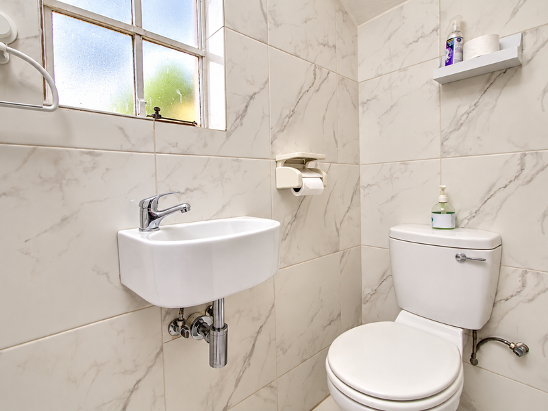 A compact, modern bathroom featuring marble-effect wall tiles, a wall-mounted basin with a chrome mixer tap, and a standard toilet.