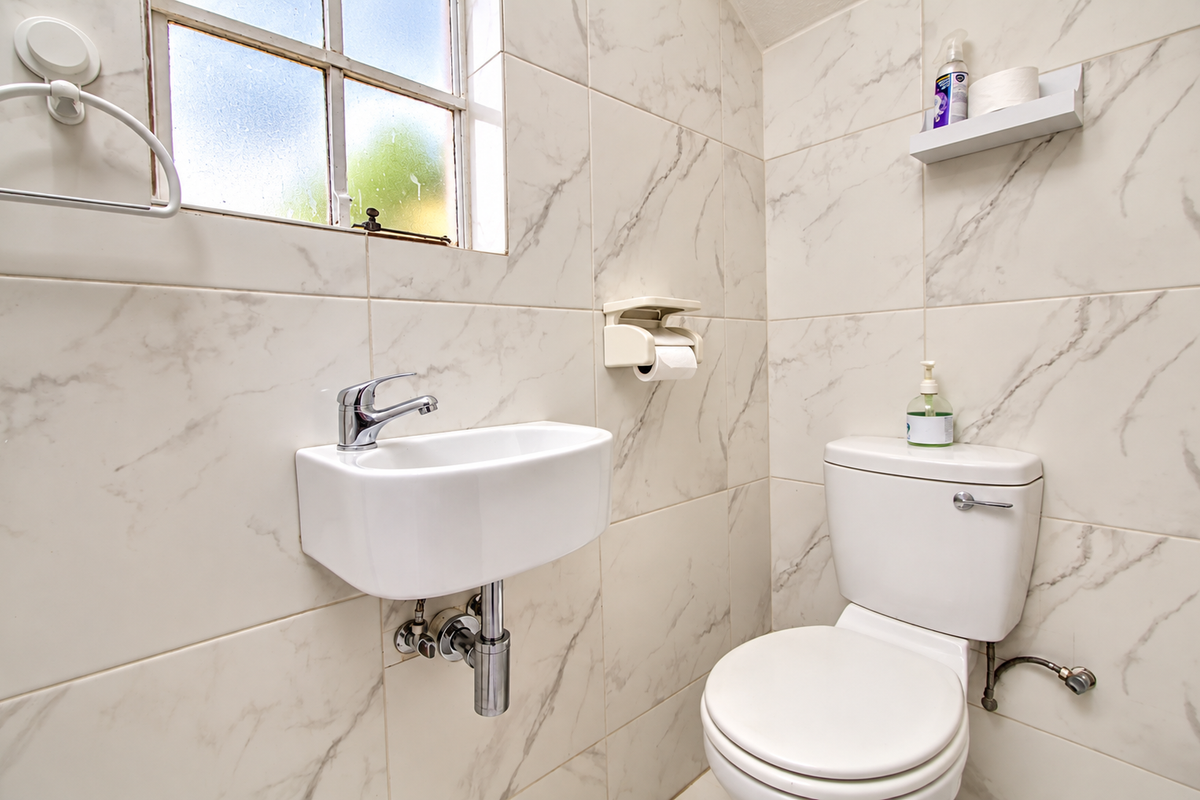 A compact, modern bathroom featuring marble-effect wall tiles, a wall-mounted basin with a chrome mixer tap, and a standard toilet.