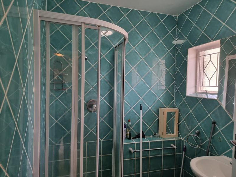 A functional bathroom featuring a corner shower enclosure, pedestal basin, and distinctive teal diamond-patterned wall tiling.