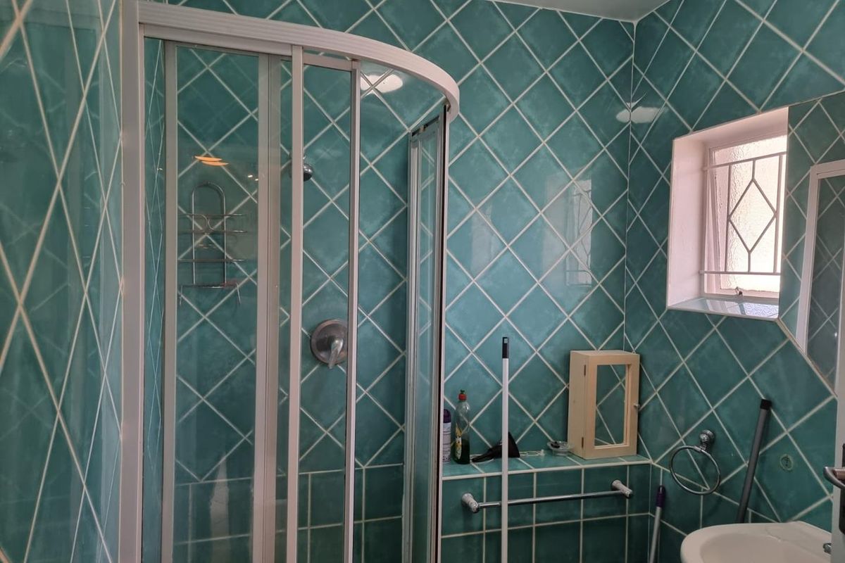 A functional bathroom featuring a corner shower enclosure, pedestal basin, and distinctive teal diamond-patterned wall tiling.