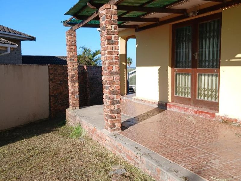 A covered outdoor patio area featuring brick pillars, tiled flooring, and a corrugated roof, providing a functional space for outdoor relaxation.
