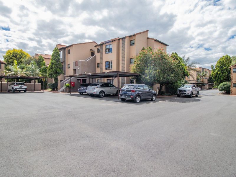 Exterior view of a multi-story apartment complex featuring paved parking areas and covered carports for residents.