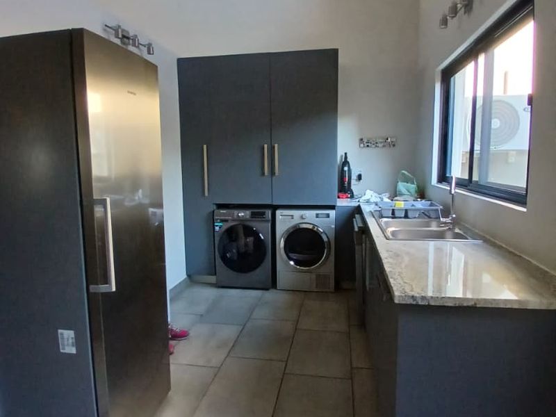 A functional laundry room featuring modern dark cabinetry, stone countertops, a stainless steel sink, and tiled flooring under a vaulted ceiling.