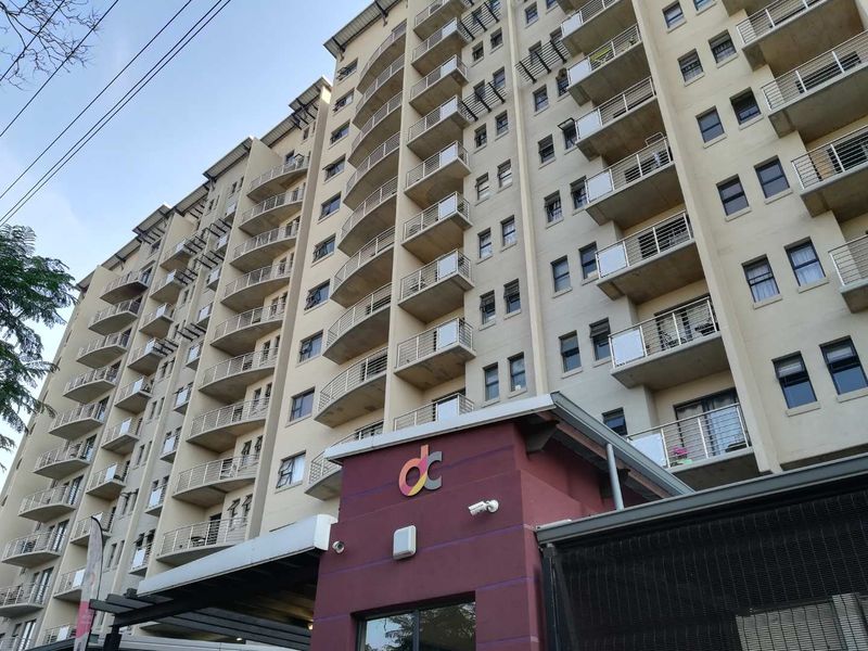 A low-angle view of a multi-story apartment building featuring numerous balconies with metal railings and a prominent entrance area.