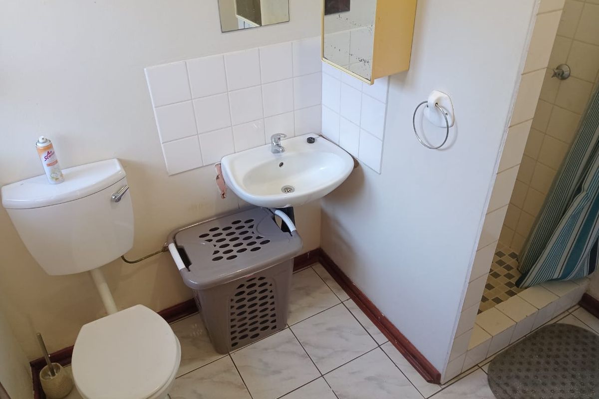A compact bathroom featuring a wall-mounted basin, a standard toilet, and a shower enclosure with tiled flooring.