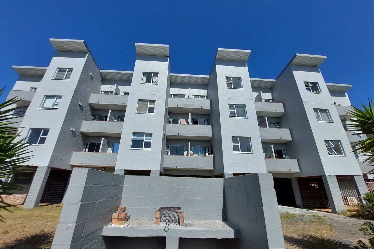 Rear view of a multi-story apartment building featuring private balconies, sliding doors, and a communal built-in braai area in the garden.