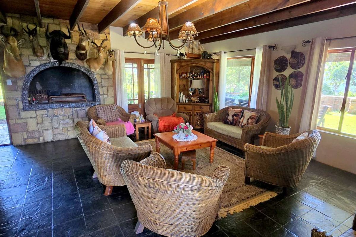 Spacious living area featuring a rustic stone fireplace, exposed timber ceiling beams, and slate tile flooring with direct access to the garden.