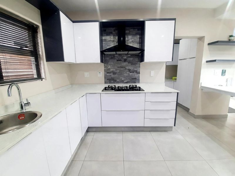 Modern kitchen featuring sleek white cabinetry, stone countertops, a gas hob with extractor fan, and a stylish stone tile splashback.