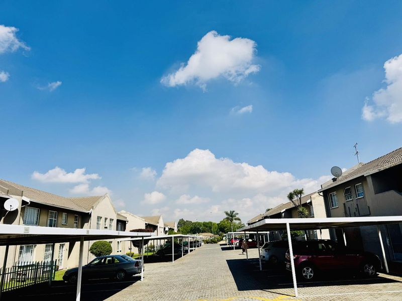 Exterior view of an apartment complex featuring a paved driveway and covered parking carports for residents.