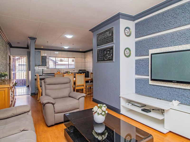 Open-plan living and dining area featuring laminate flooring, a textured feature wall, and an adjoining kitchen with breakfast counter and built-in cabinetry.