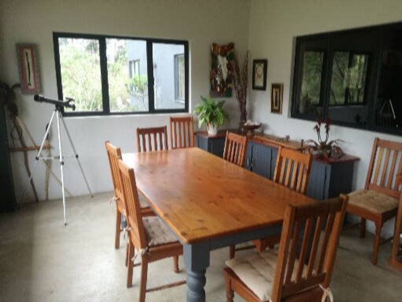 A dining room featuring concrete flooring and large aluminium-framed windows, providing a functional space for family meals.