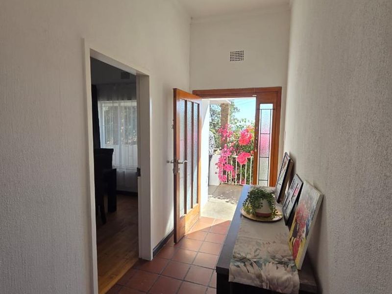 A bright hallway featuring terracotta floor tiles and a glass-panelled door leading to an outdoor area.