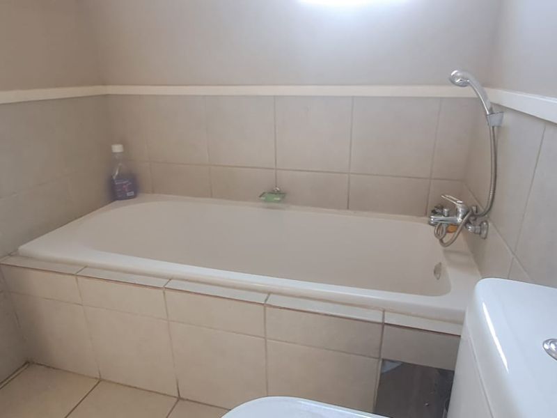 A functional bathroom featuring a built-in bathtub with a handheld shower attachment and neutral ceramic tiling throughout.
