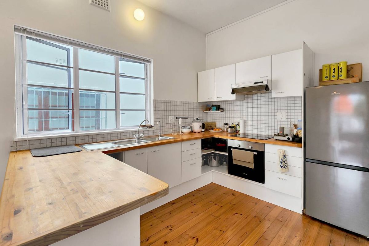 A functional kitchen featuring white cabinetry, timber countertops, a tiled splashback, and warm timber flooring, offering a bright and practical workspace.