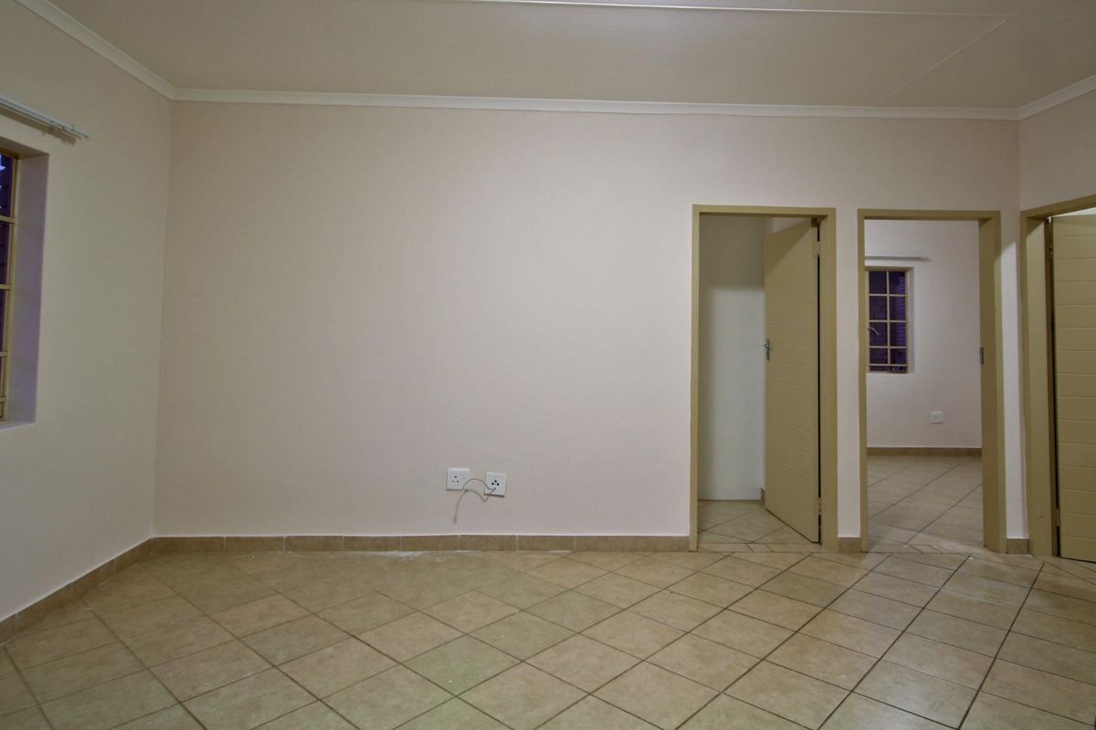 An empty bedroom featuring neutral walls, tiled flooring, and access to adjacent rooms through internal doors.