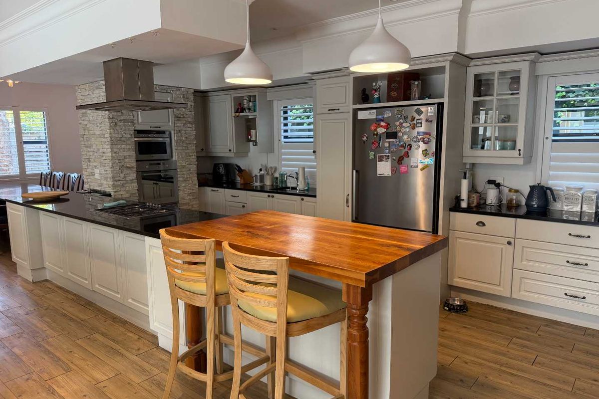 A well-appointed kitchen featuring a large island with a wooden breakfast bar, stone countertops, built-in oven, extractor fan, and ample cabinetry.