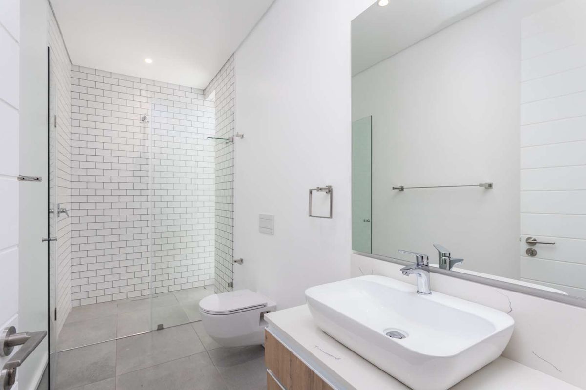 A modern, minimalist bathroom featuring a walk-in shower with subway tiles, a wall-mounted toilet, and a sleek vessel sink vanity.