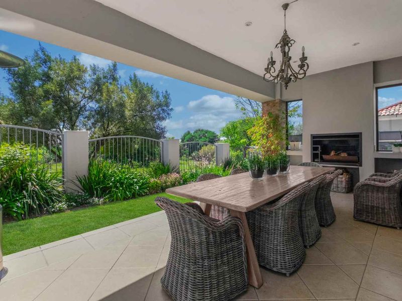 A spacious covered patio featuring a built-in fireplace, tiled flooring, and direct access to a landscaped garden with metal perimeter fencing.