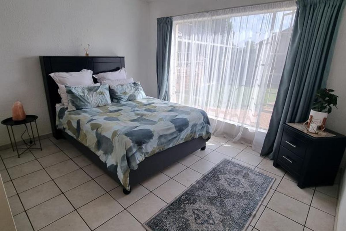 A well-lit bedroom featuring large windows with curtains, tiled flooring, and a ceiling-mounted light fixture.