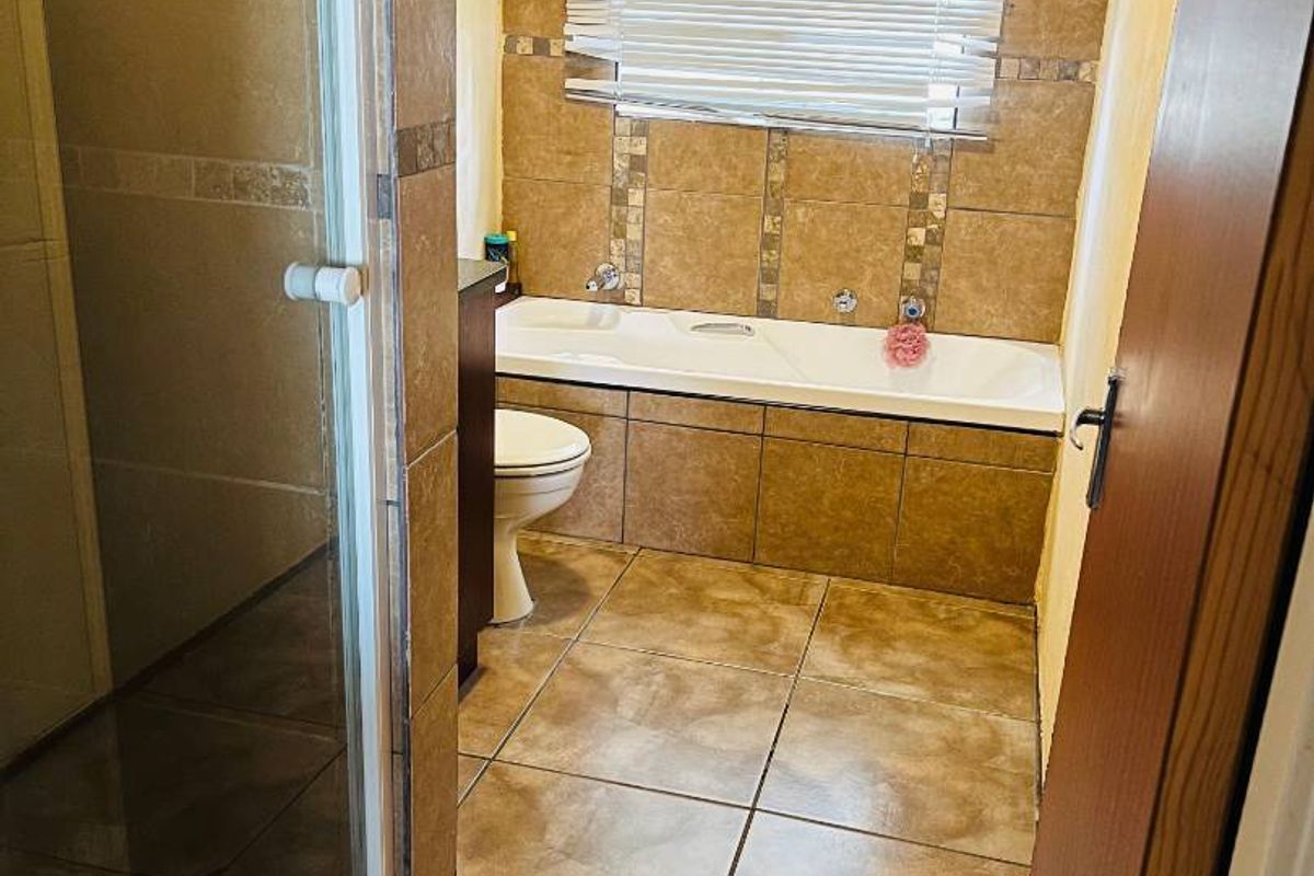 A functional bathroom featuring a built-in bathtub, a separate shower enclosure, and full-height wall tiling.