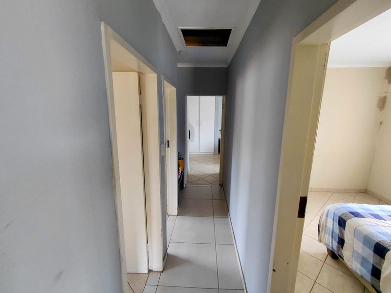 A functional hallway featuring tiled flooring and a ceiling access hatch, providing access to adjacent rooms within the property.