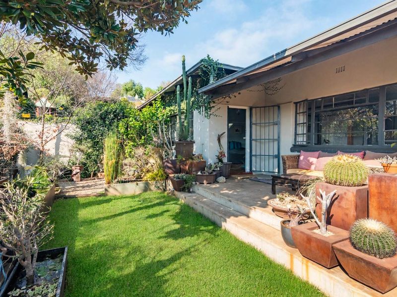 A charming covered patio area overlooking a landscaped garden, featuring concrete flooring and direct access to the home through a security gate.