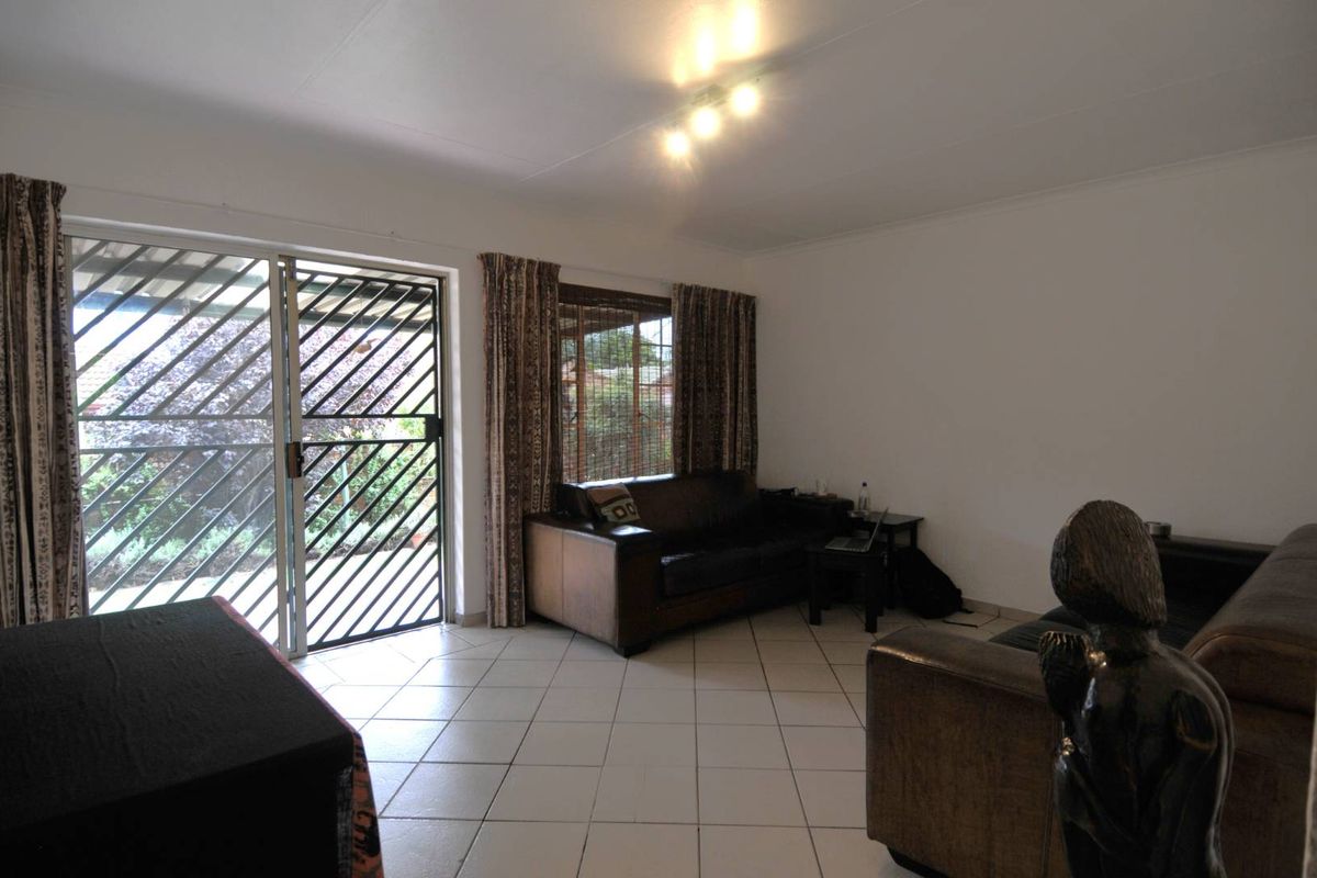 A living room featuring tiled flooring, large sliding glass doors with security gates, and access to an outdoor patio area.
