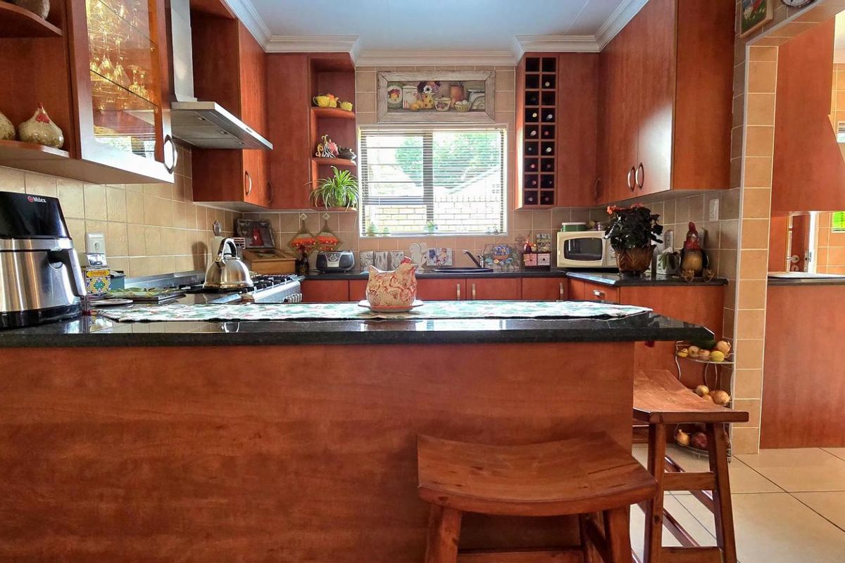 A functional kitchen featuring wooden cabinetry, granite countertops, a breakfast bar, and tiled splashbacks, with an adjacent tiled transition area.