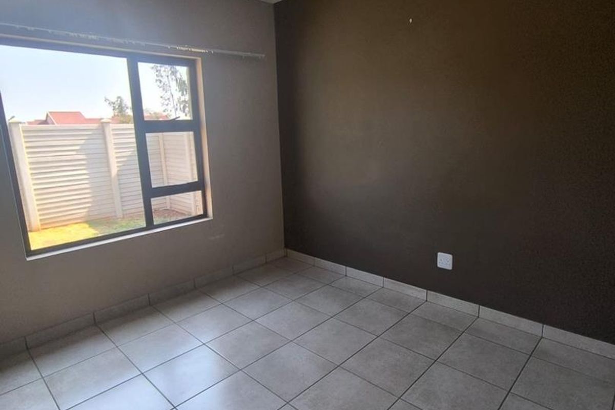 An empty bedroom featuring neutral tiled flooring, a dark accent wall, and an aluminium-framed window providing natural light.