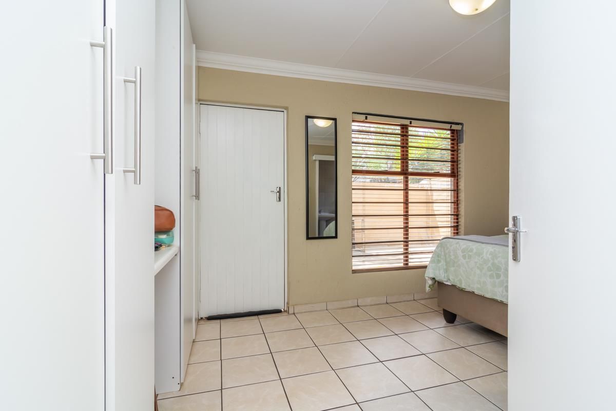 A bedroom featuring tiled flooring, built-in cupboards, and a window with wooden blinds, providing a functional and well-lit living space.