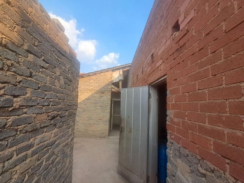 Exterior view of a rear courtyard area featuring exposed brick walls and a metal door, showing significant signs of structural wear and deterioration.