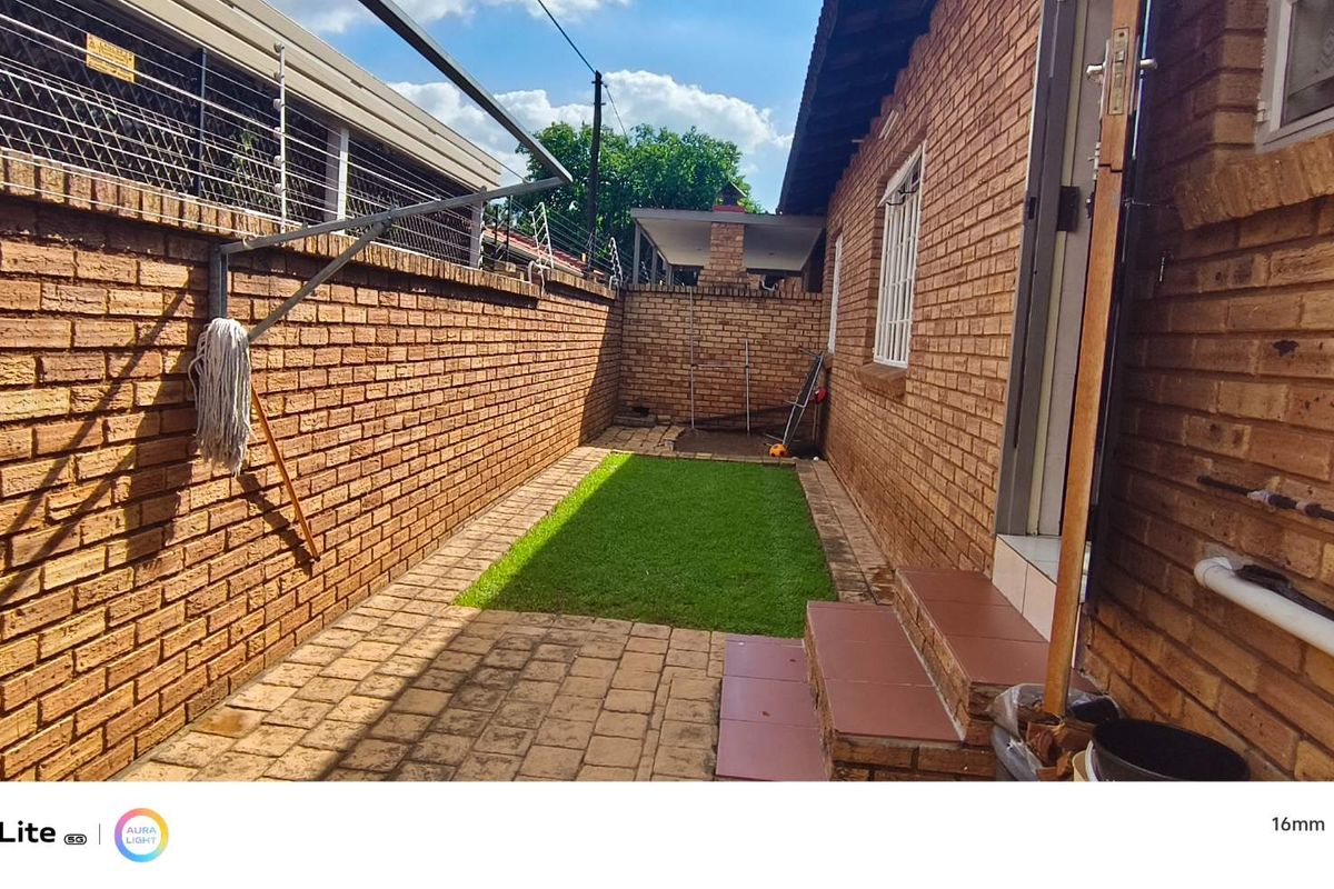 A private rear courtyard featuring face brick walls with electric fencing, a small lawn area, and paved flooring with tiled steps leading to the entrance.
