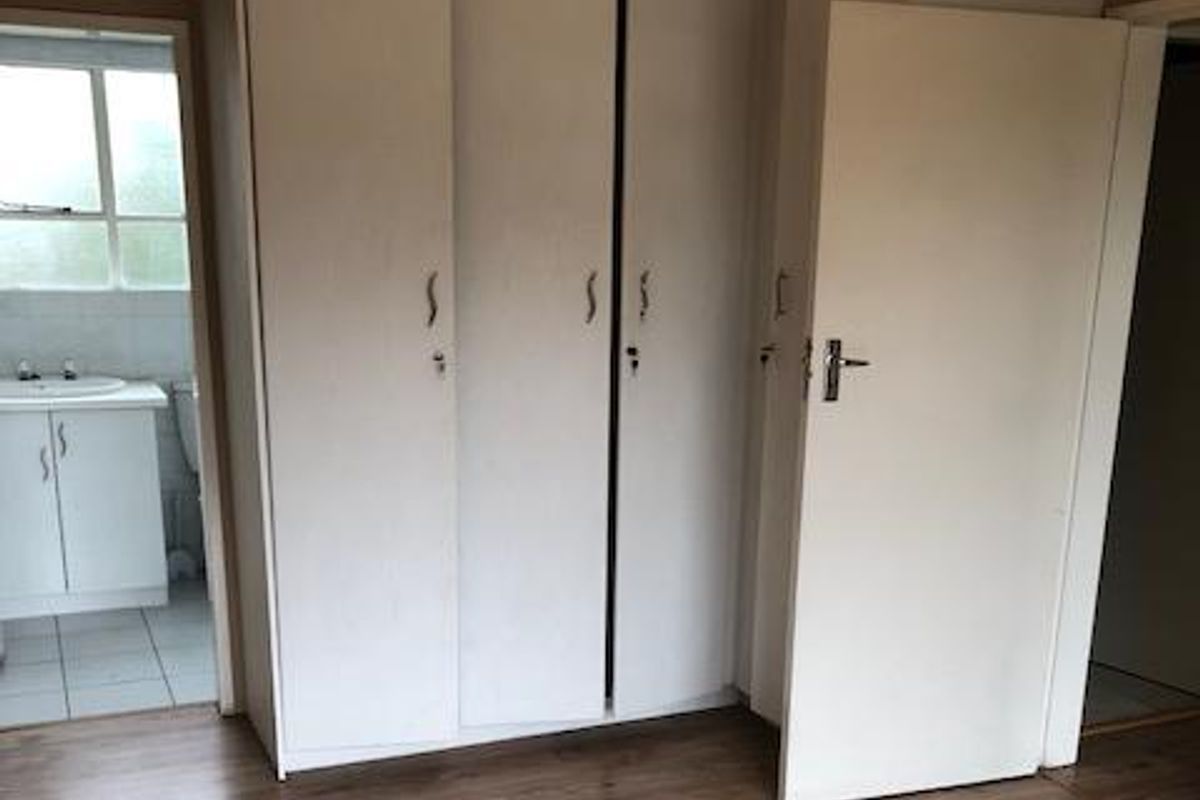 A bedroom featuring built-in white wardrobes and laminate flooring, with an adjacent en-suite bathroom visible through the doorway.