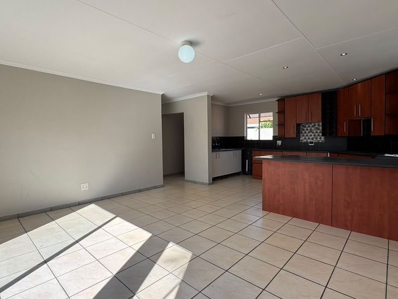 Spacious open-plan living and kitchen area featuring tiled flooring, built-in wooden cabinetry, and a functional kitchen island layout.