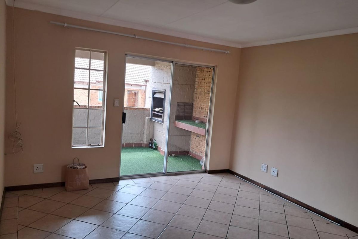 An empty living area featuring tiled flooring and sliding glass doors that open onto a private balcony with a built-in braai.