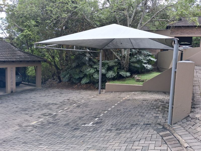 Outdoor parking area featuring a paved driveway and a shade sail carport structure, set within a landscaped residential environment.