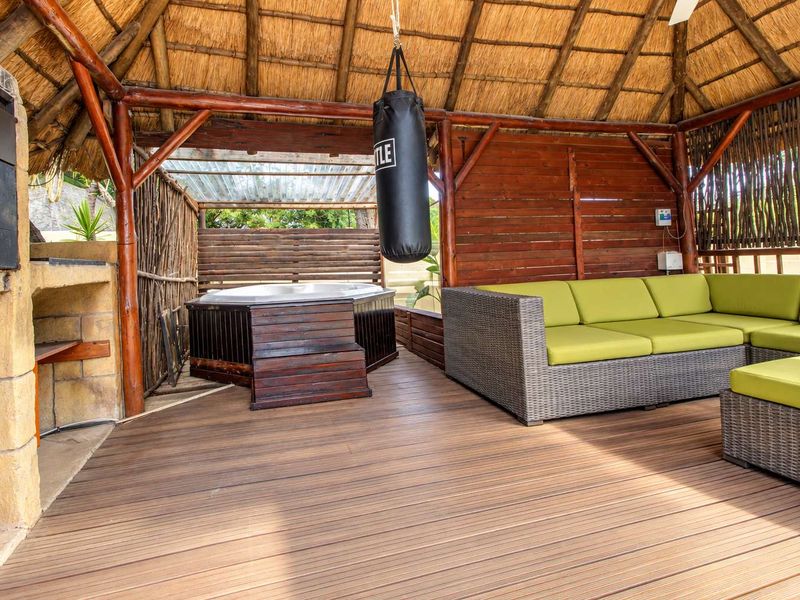 Covered outdoor entertainment area featuring a thatched roof, timber decking, built-in braai, and a private jacuzzi.