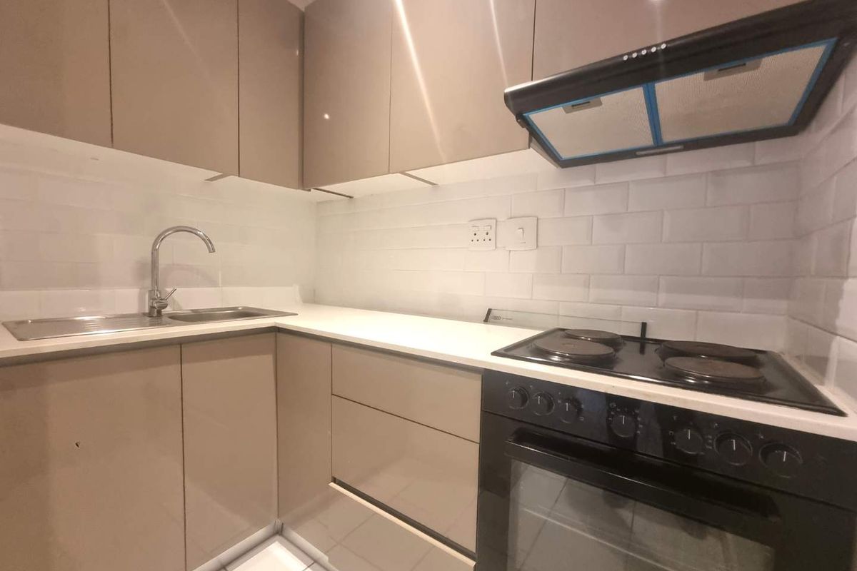 A modern, compact kitchen featuring high-gloss cabinetry, a subway tile backsplash, integrated electric hob, oven, and extractor fan with a clean countertop finish.
