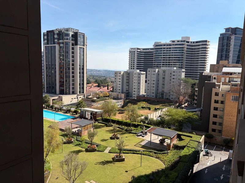 Elevated urban view overlooking a well-maintained residential complex featuring a swimming pool, landscaped gardens, and paved communal areas.