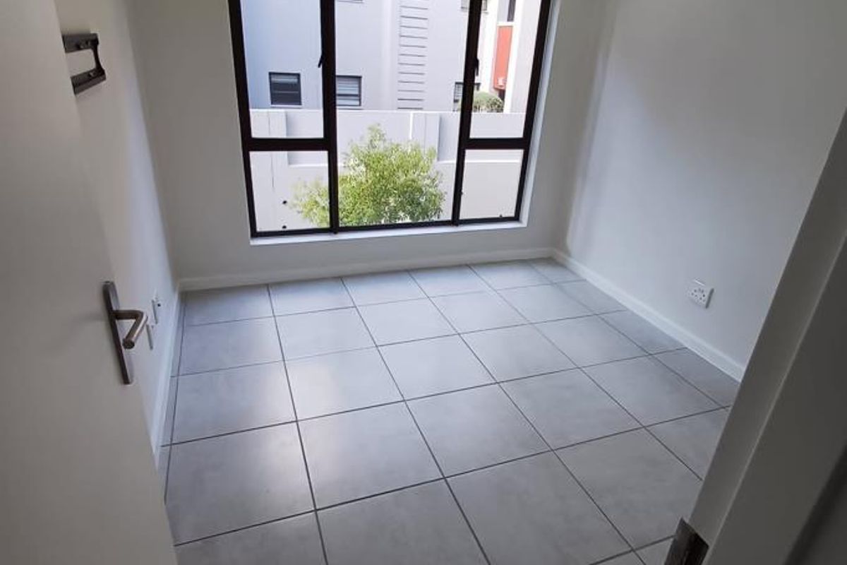 A bright, empty bedroom featuring large windows, neutral tiled flooring, and a clean, modern finish, ready for personalization.