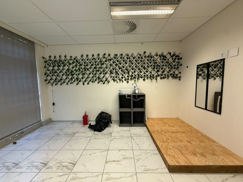 Office space featuring tiled flooring, suspended ceiling with integrated lighting, air conditioning, and a small wall-mounted basin area.