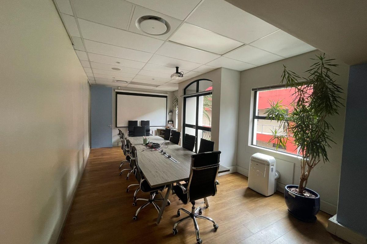 A functional office boardroom featuring laminate flooring, a suspended ceiling with recessed lighting, a projector screen, and large windows providing natural light.