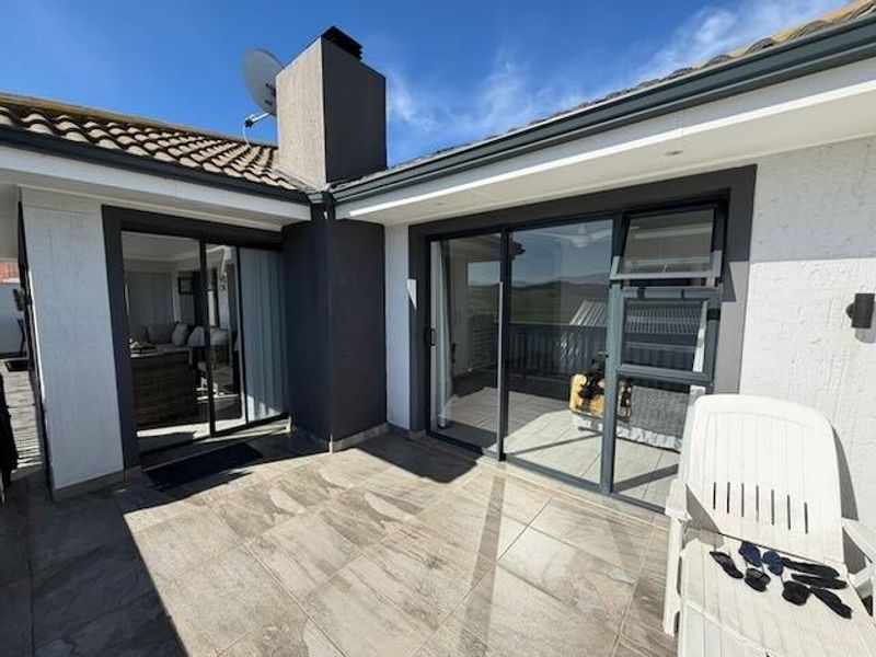 A modern covered patio area featuring tiled flooring, recessed lighting, and large sliding glass doors providing seamless access to the interior living space.
