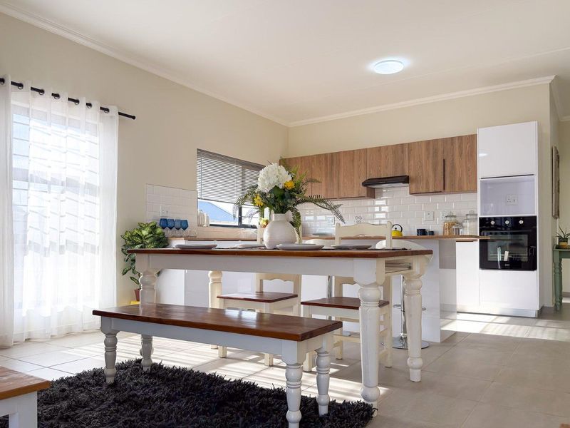 A bright open-plan kitchen and dining area featuring modern white and wood-grain cabinetry, subway tile backsplash, and integrated oven.