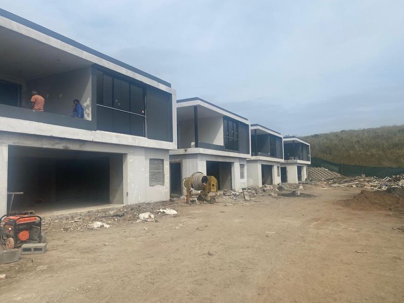 A row of modern residential units currently under construction, featuring concrete structures, balconies, and sliding glass doors in an unfinished state.