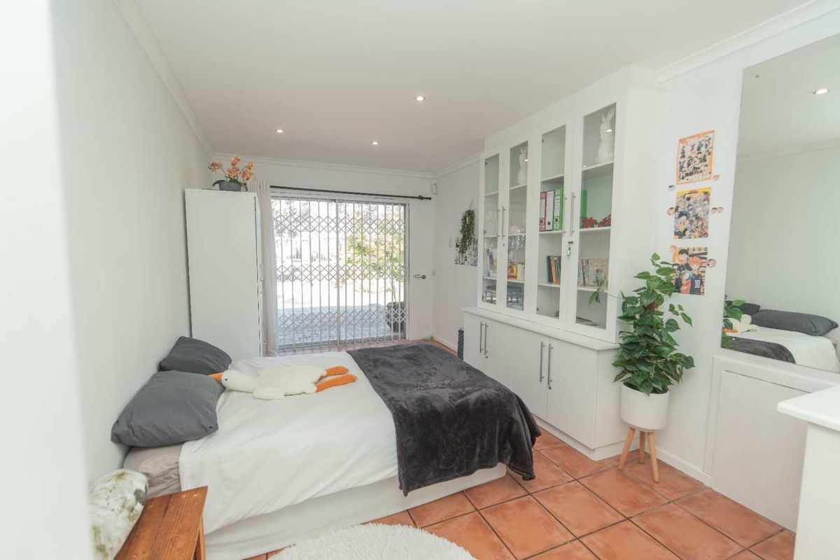 A bedroom featuring built-in cabinetry, tiled flooring, and a sliding glass door with security gate leading to the exterior.